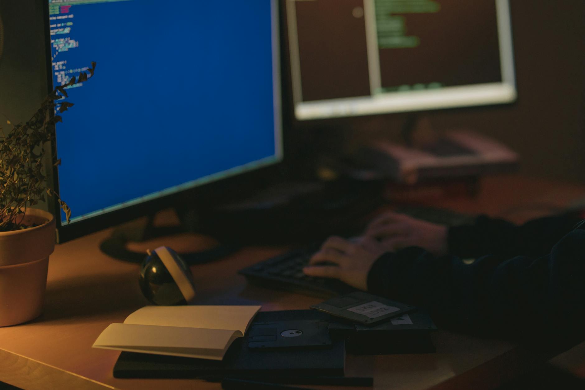 Programista pracuje przy dwóch monitorach w ciemnym pomieszczeniu