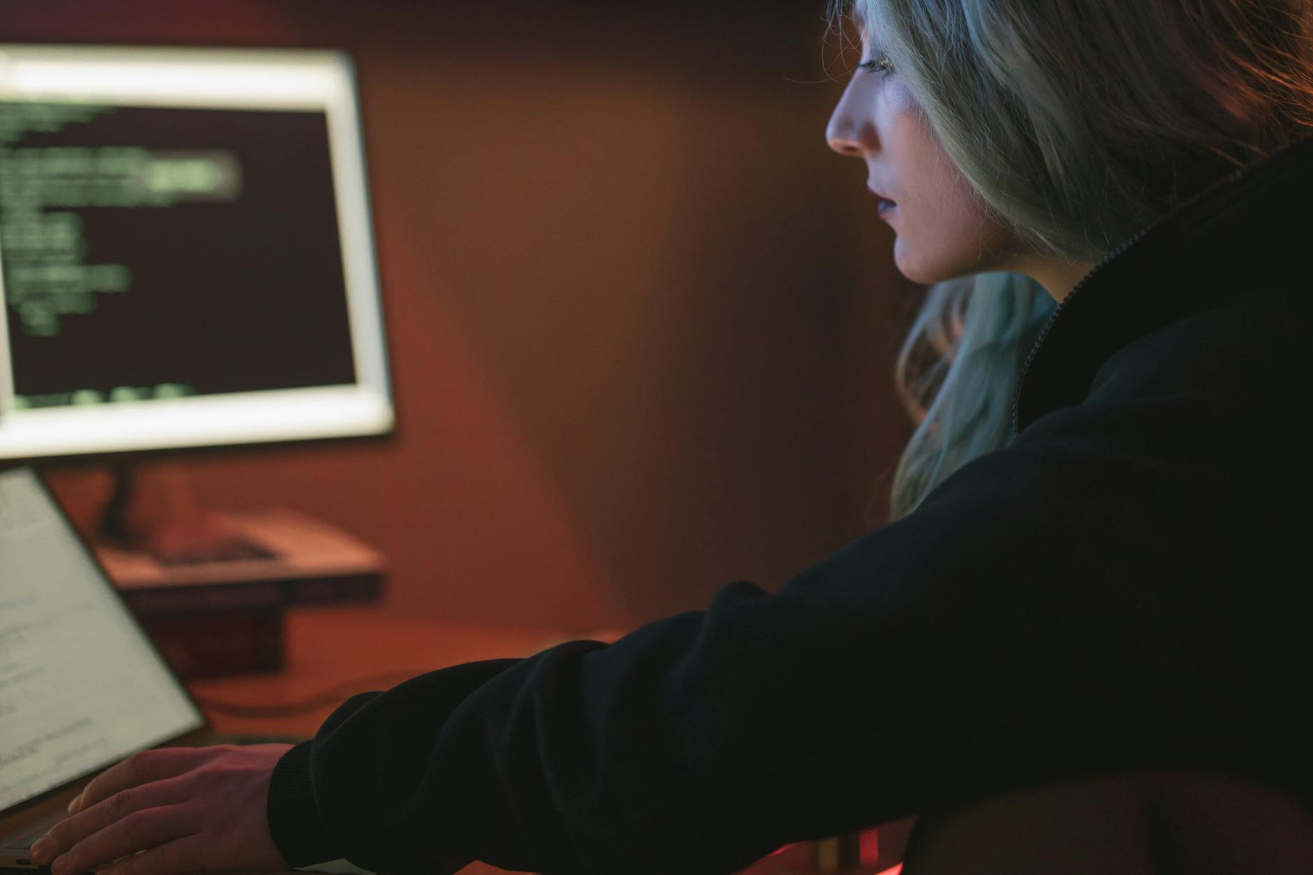 Programistka pracuje nocą przy laptopie z kodem w ciemnym pokoju